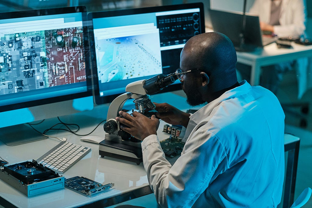 Man inspecting PCB for defects with a microscope.